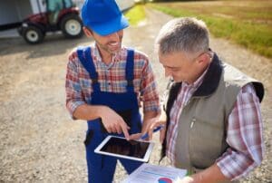 Farmer and consultant discussing data on a tablet outdoors.